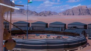 A desert camp with striped tents and a flagpole with a flag. - Desert Sand Camp (Wadi Rum)