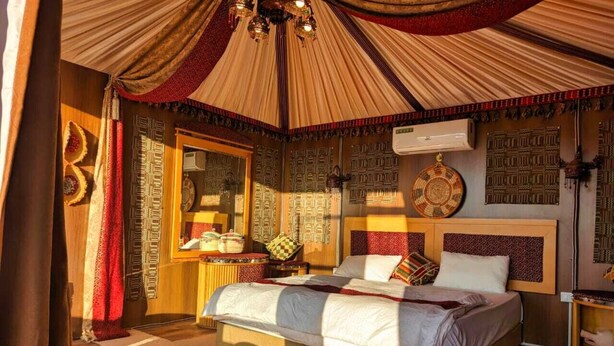 A bedroom with a large bed, a mirror, patterned wall decorations, and a ceiling fan. - Desert Sand Camp (Wadi Rum)