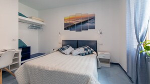 A modern bedroom with a bed, a desk, and a chair. There is a painting above the bed and a plant on the right. - VIAPARSANO - two bedrooms flat (Sorrento)