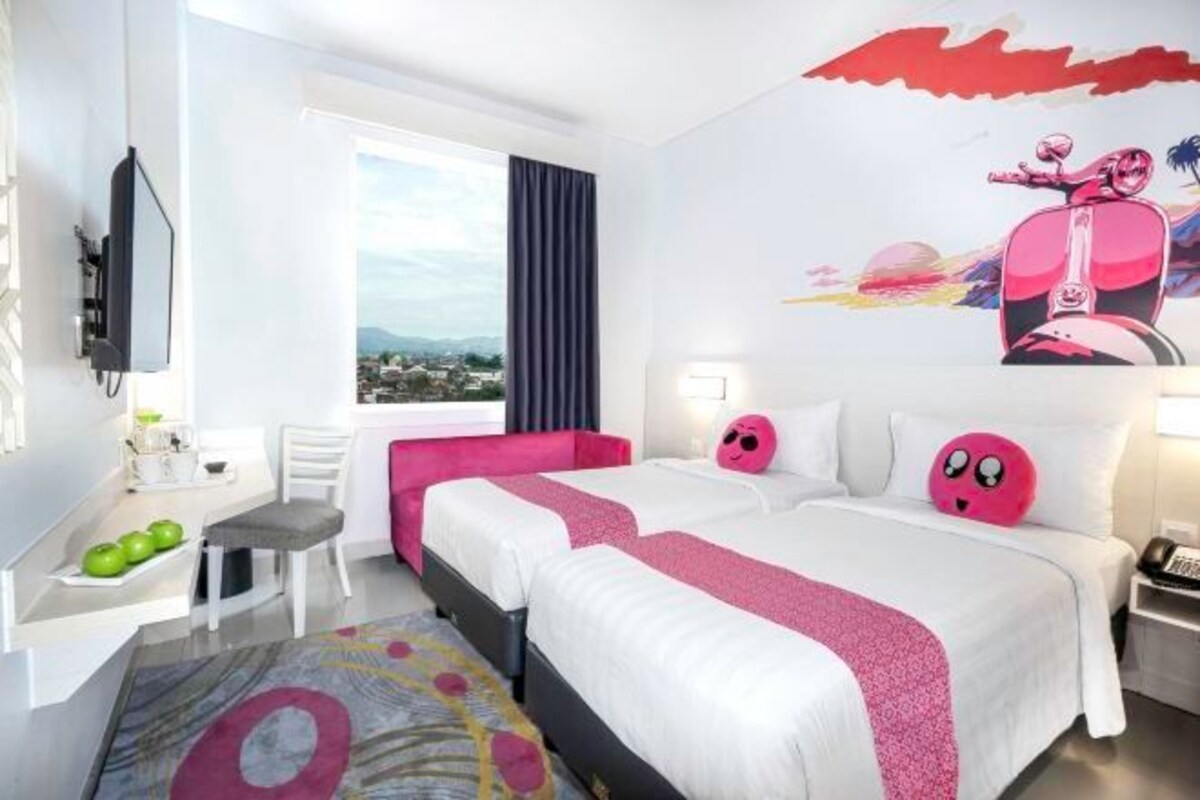 A hotel room with two beds, a desk with a chair, a window with a view, and a wall with a mural.