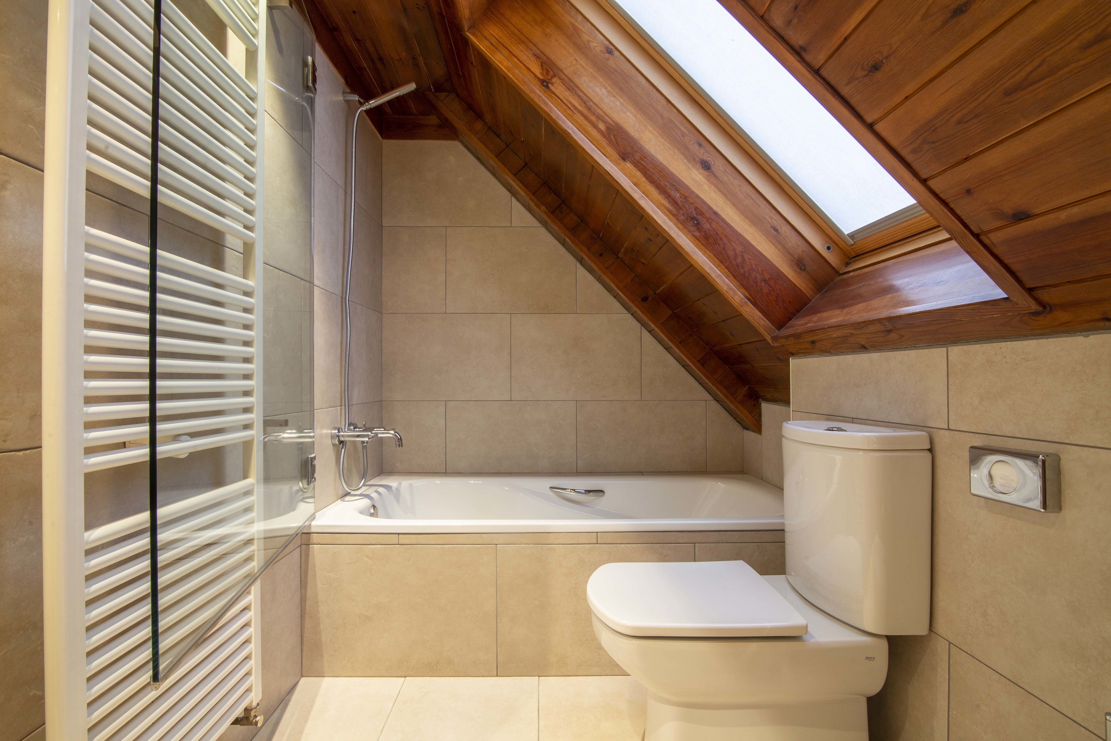 A bathroom with a bathtub, toilet, and a skylight.
