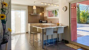 A modern kitchen with a central island, bar stools, and a large window offering a view of greenery. - Gorgeous home in Creissan (Creissan)