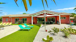 A modern house with a red exterior, a covered patio with green chairs, and a well-maintained lawn. - Gorgeous home in Creissan (Creissan)