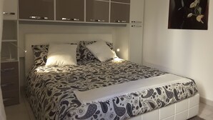 Un dormitorio con cama, mesita de noche, cómoda y un cuadro en la pared.