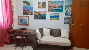 Una habitación pequeña con un sofá, una mesa de comedor con sillas y una pared decorada con varias pinturas.
