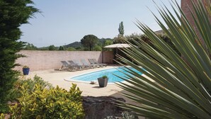 A pool area with lounge chairs, a small umbrella, and potted plants.