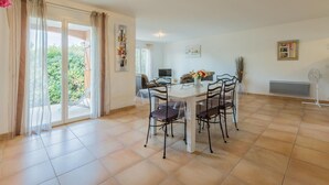 A dining area with a table and chairs, a TV, and a view of greenery outside.