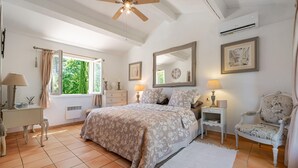 Une chambre à coucher avec un lit, des tables de chevet, une chaise, une fenêtre et un ventilateur de plafond.