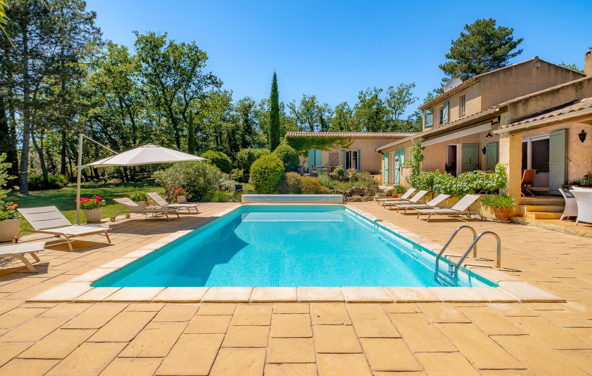 A rectangular swimming pool with a tiled deck, surrounded by lounge chairs and umbrellas.