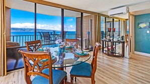 Ein Essbereich mit Glastisch und Stühlen, Blick auf das Meer und ein Balkon mit Geländer.