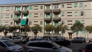 Un immeuble résidentiel à plusieurs étages, doté de balcons, avec des voitures garées devant et des arbres.
