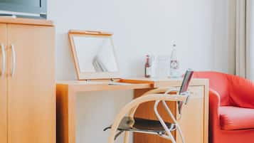 A hotel room with a wooden desk, a red chair, a mirror, and a laptop.