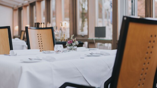 Un comedor con mesas dispuestas para una comida, sillas y un jarrón con flores.