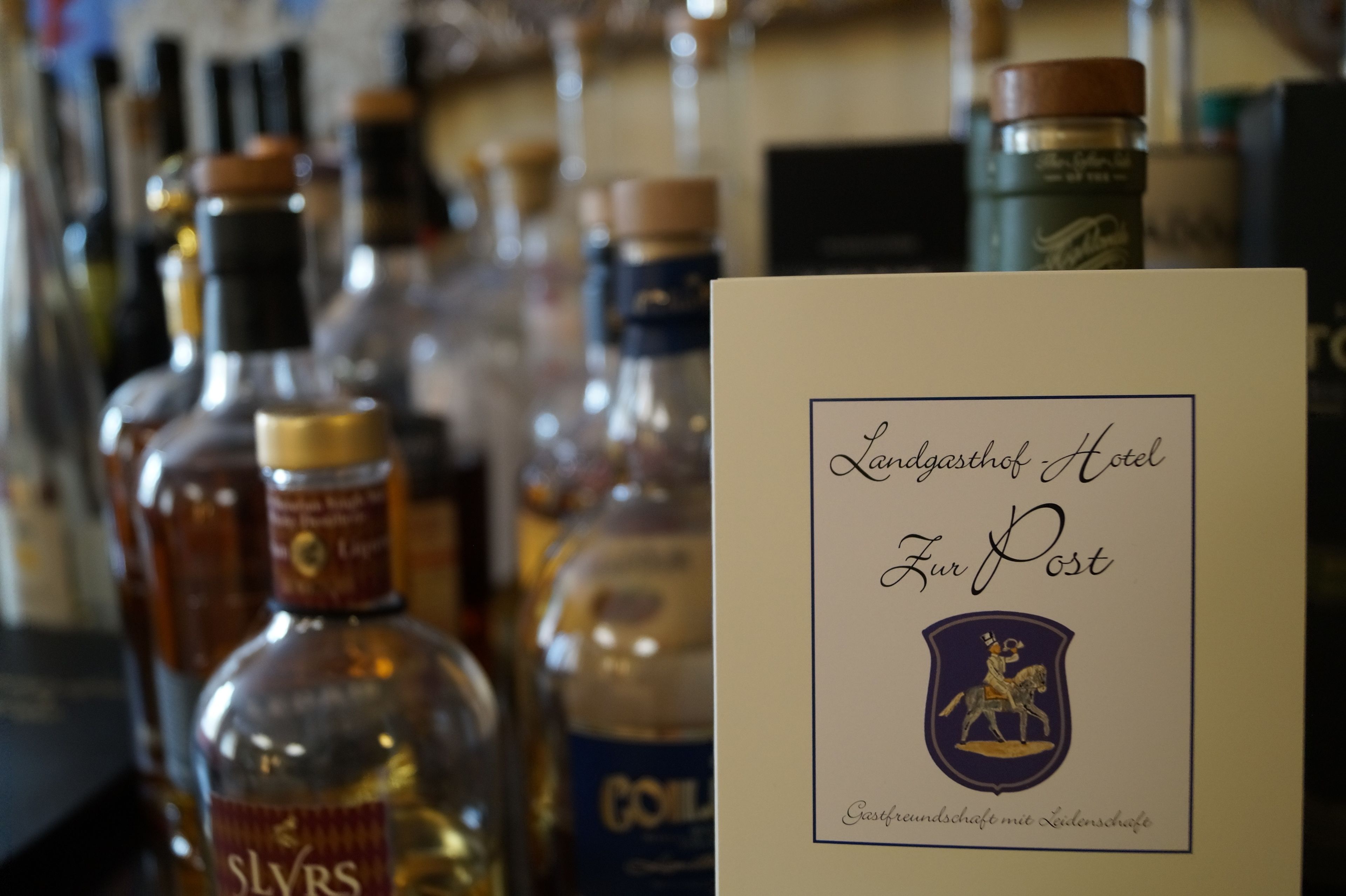 Zona de bar con diversas botellas de licores y un cartel que dice "Landgasthof Hotel Für Post" con un escudo de armas.