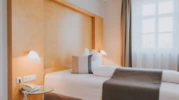 Una habitación de hotel con una cama grande, lámparas de noche, un teléfono y una ventana con cortinas.