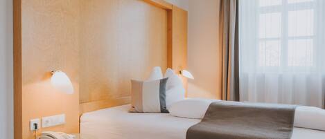 A hotel room with a large bed, bedside lamps, a telephone, and a window with curtains.