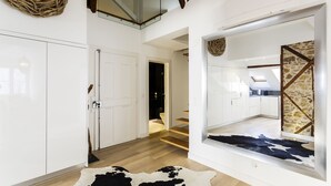 A modern interior with a wooden staircase, white cabinetry, and a large mirror reflecting a kitchen area. - Madalena Downtown Luxury Duplex (Lisbon)