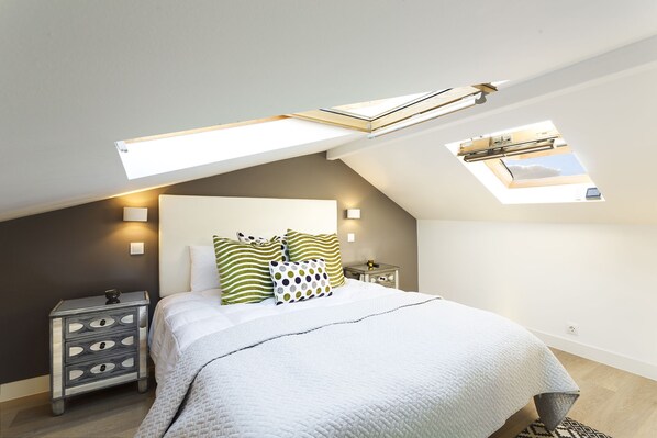 A bedroom with a skylight, a bed with white bedding, and a nightstand with drawers.