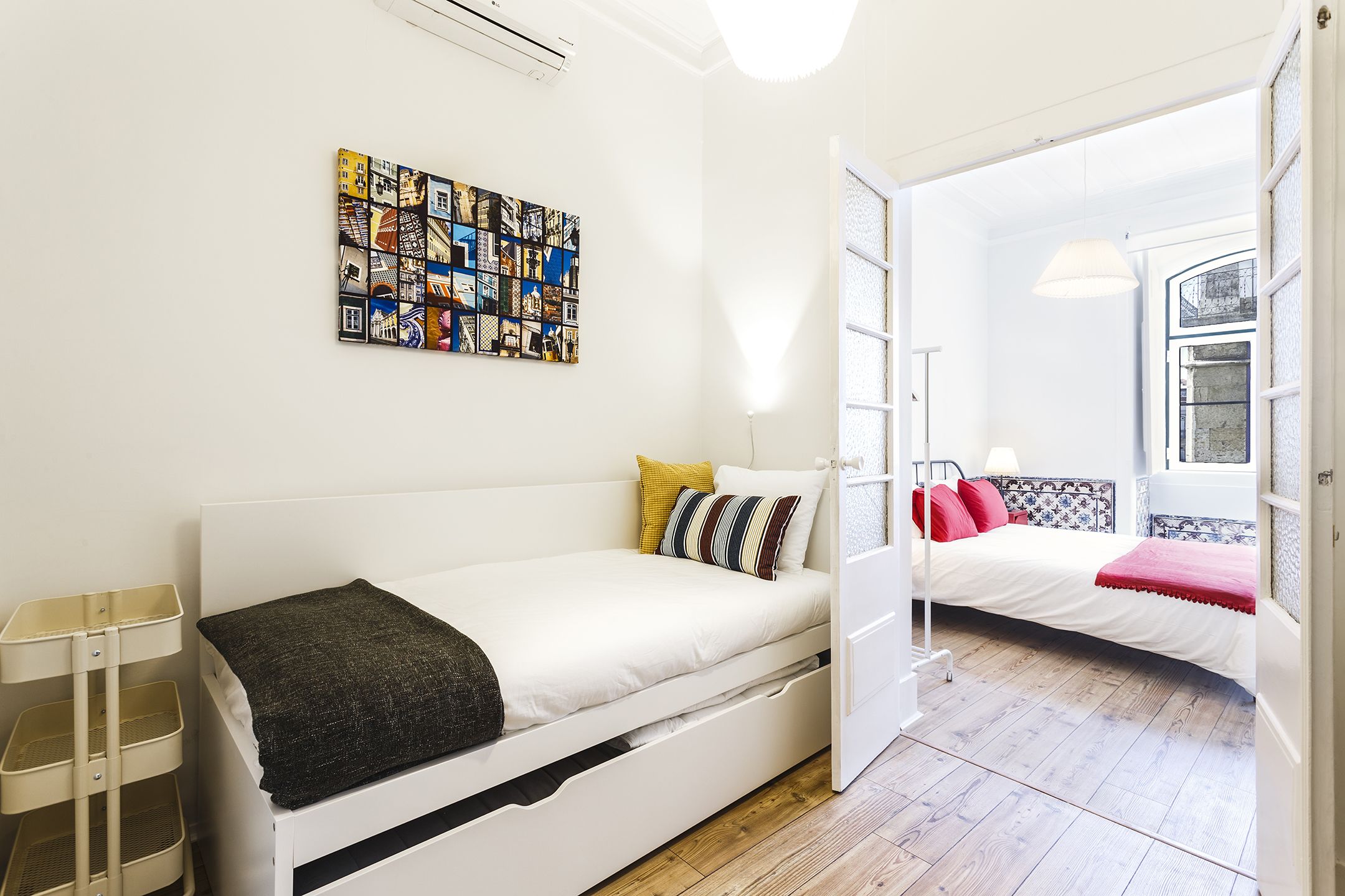 Een moderne, goed verlichte kamer met een wit bed, een klein nachtkastje en een kleurrijk kunstwerk aan de muur.