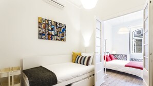 A modern, well-lit room with a white bed, a small side table, and a colorful artwork on the wall. - Fanqueiros Deluxe Apartment (Lisbon)