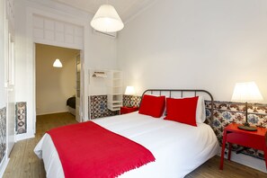 A neatly arranged bedroom with a large bed, two bedside tables with lamps, a wardrobe, and a door leading to another room. - Fanqueiros Deluxe Apartment (Lisbon)