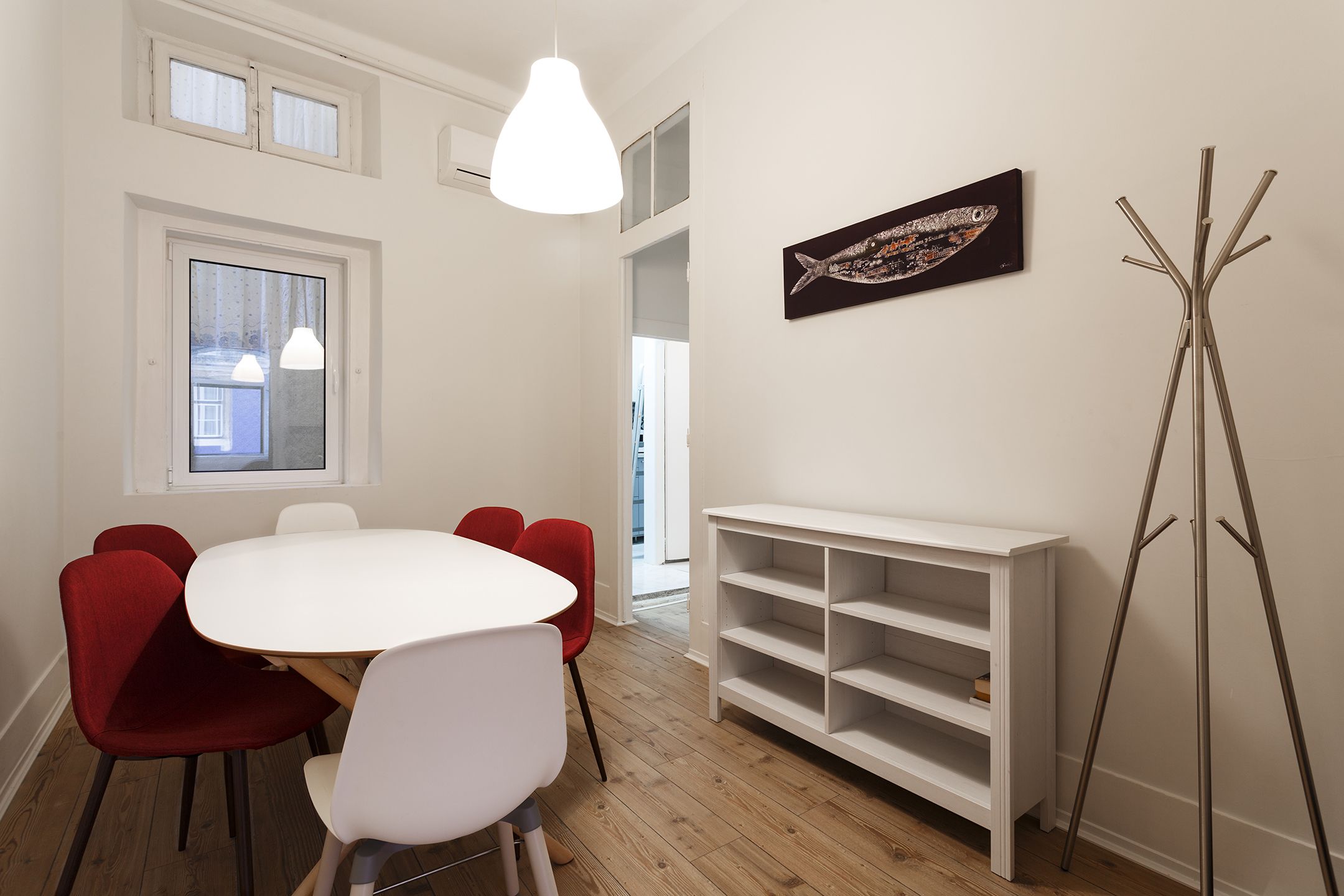 A dining area with a white table and red chairs, a white console table, and a fish painting on the wall.