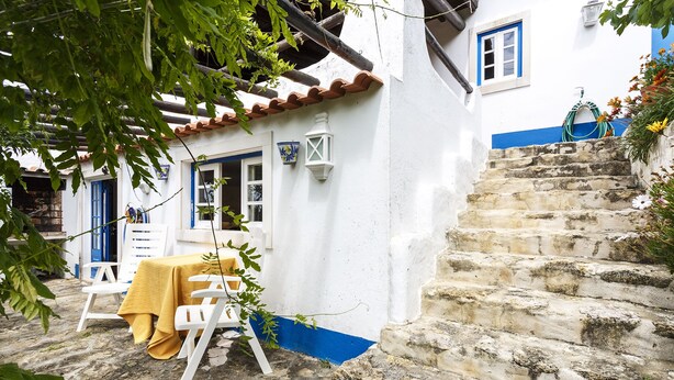 Un edificio blanco con detalles azules, una escalera de piedra y una mesa con mantel amarillo.