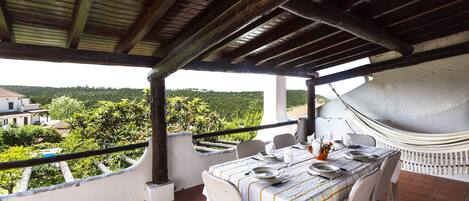 A covered outdoor dining area with a table set for two, overlooking a scenic landscape.