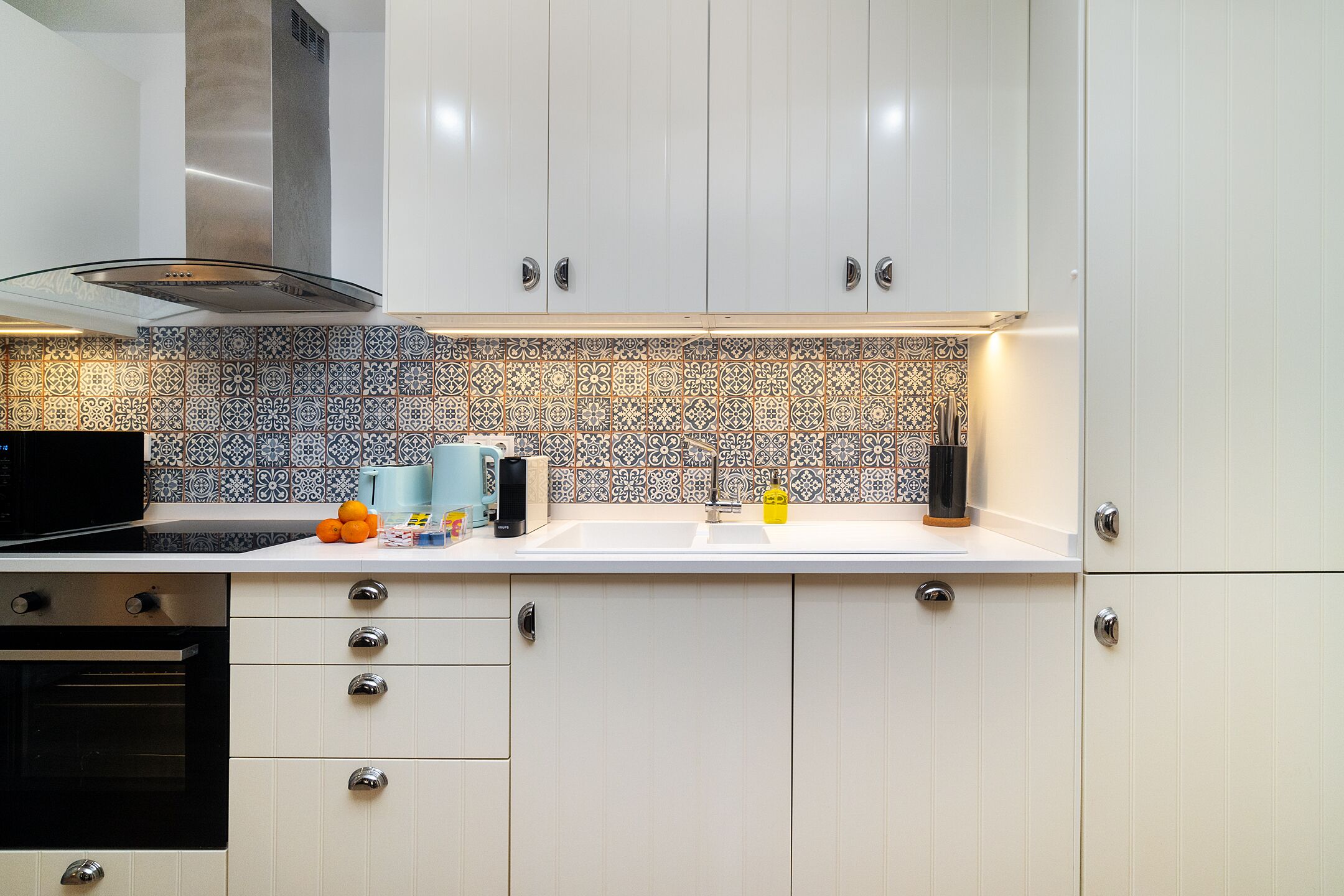 A modern kitchen with white cabinets, a patterned backsplash, and stainless steel appliances.