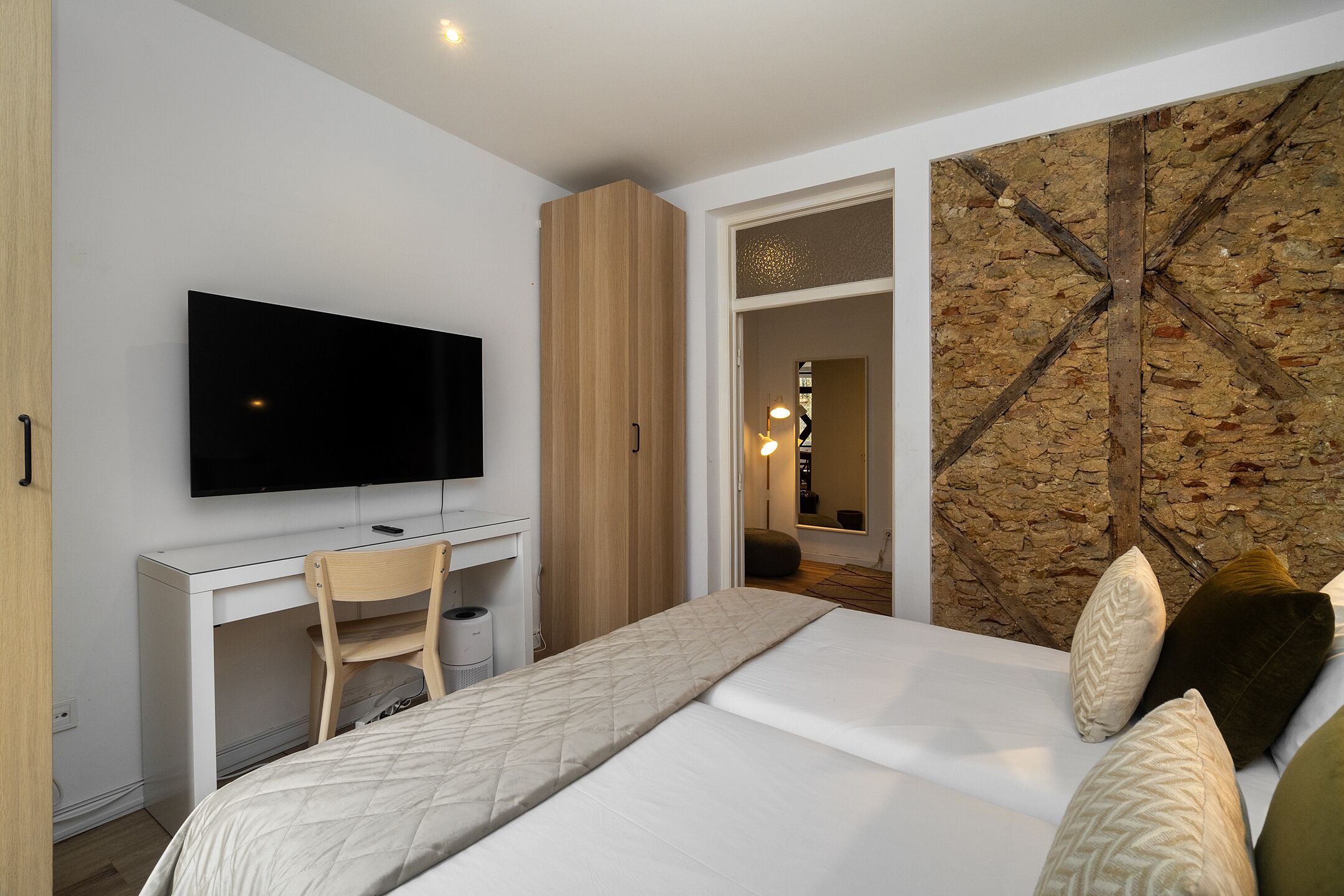A bedroom with a bed, a desk, a TV, and a stone wall.