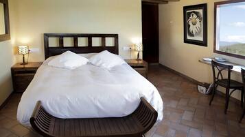 Un dormitorio con una cama grande, dos mesitas de noche con lámparas, un banco de madera, un escritorio con una silla y un cuadro enmarcado en la pared.