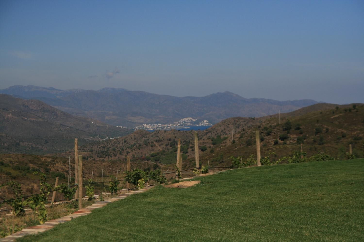 Un paisaje rural con un sendero despejado que lleva a un pueblo lejano, rodeado de colinas y vegetación escasa.