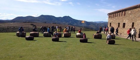 A grassy field with large cylindrical objects, a stone building, and mountains in the background.