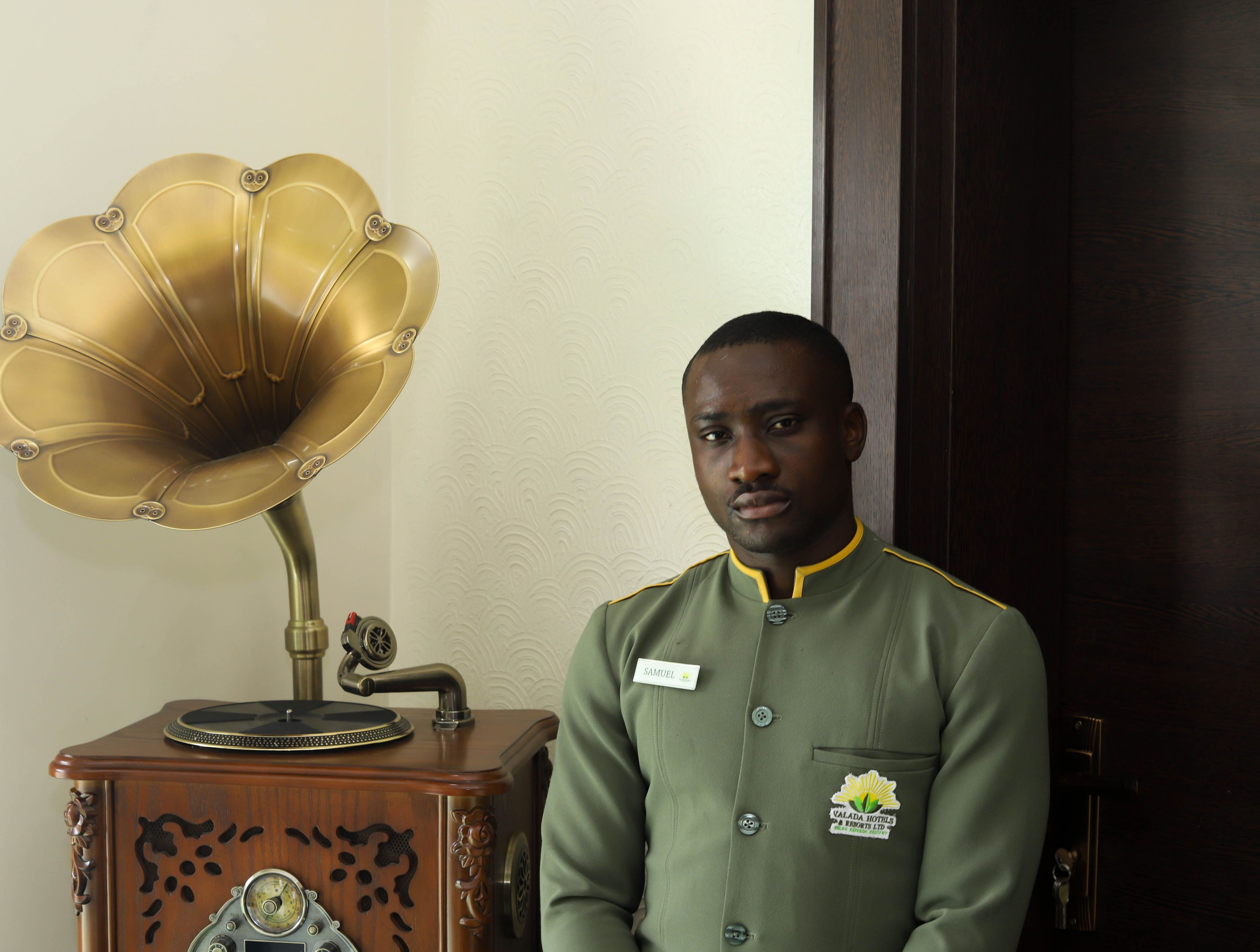 Un hombre con uniforme verde y una placa de identificación, de pie junto a un tocadiscos antiguo.