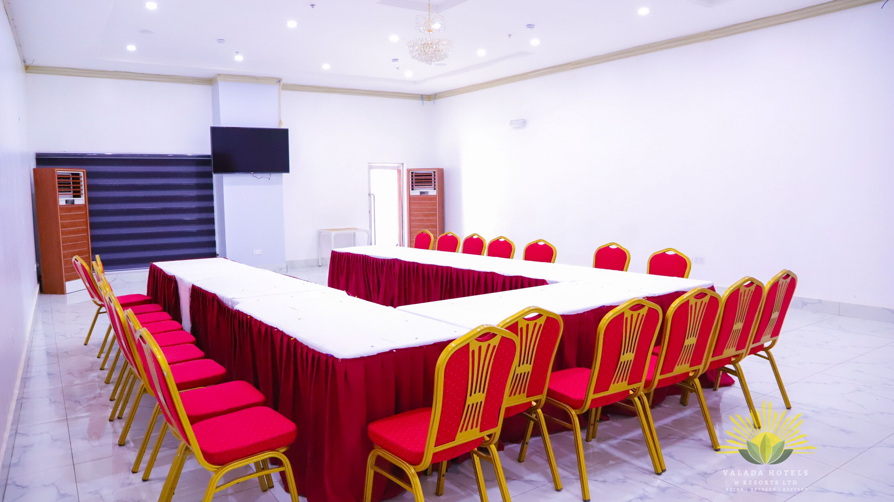A conference room with a long table, red chairs, and a TV mounted on the wall.