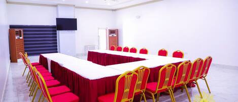 A conference room with a long table, red chairs, and a TV mounted on the wall.