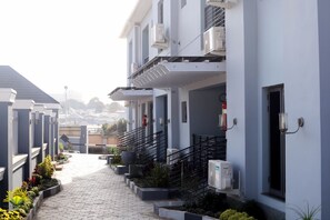 Un edificio residencial con un sendero pavimentado, iluminación exterior y unidades de aire acondicionado.