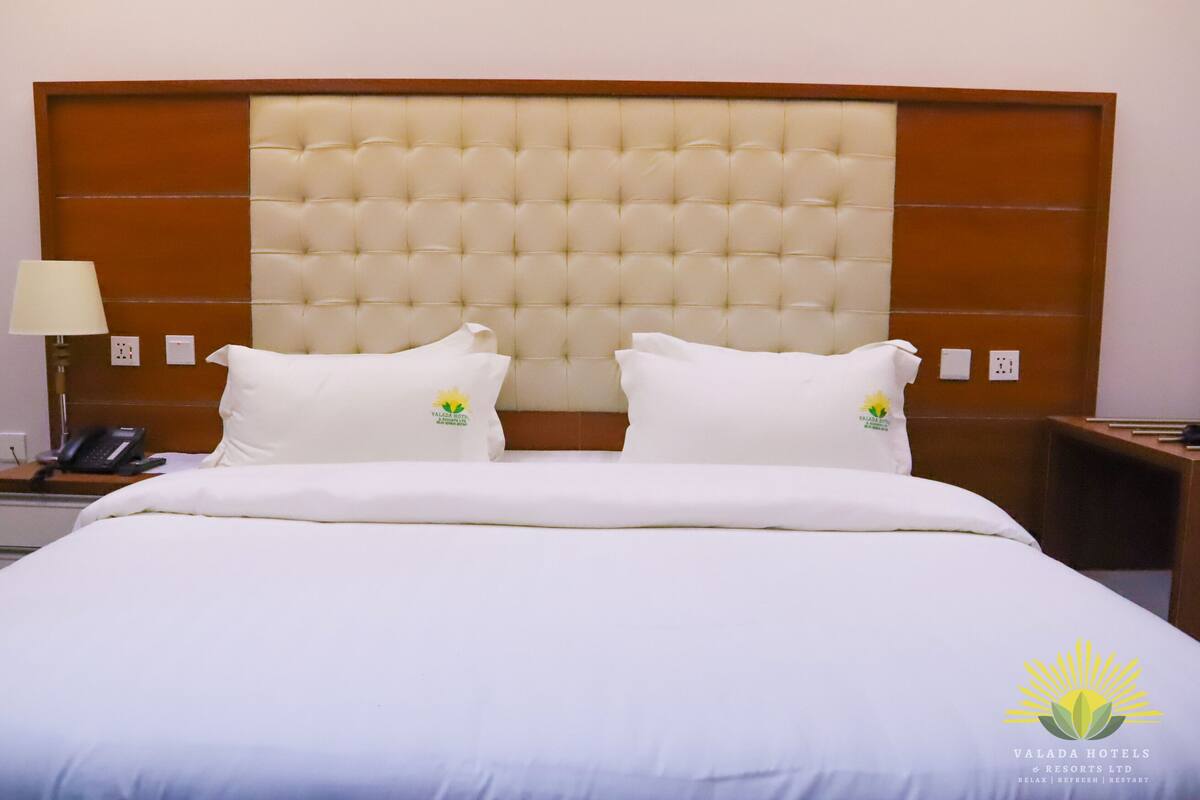 A hotel room with a large bed, two pillows, a bedside lamp, a phone, and a nightstand.
