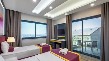 Habitación de hotel con dos camas, un escritorio, una silla y un balcón con vista a la ciudad.