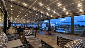 Un ristorante moderno con una lunga sala da pranzo, ampie finestre e vista sulla città.