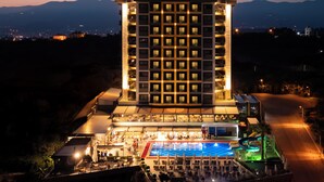 Un hotel di grandi dimensioni con numerosi piani, una piscina sul tetto e vista su montagne lontane.