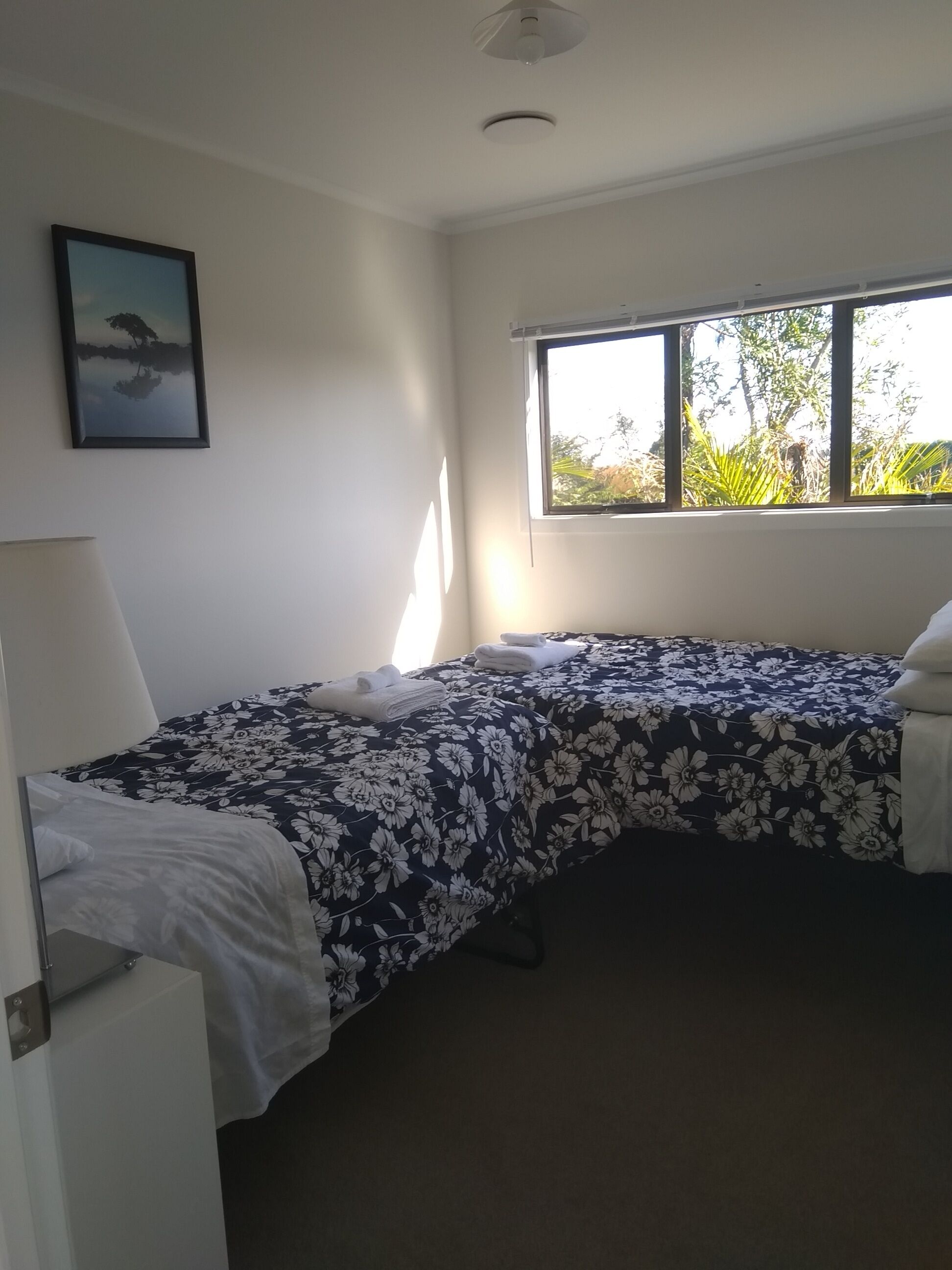 A bedroom with a bed, a window, a picture on the wall, and a ceiling light.