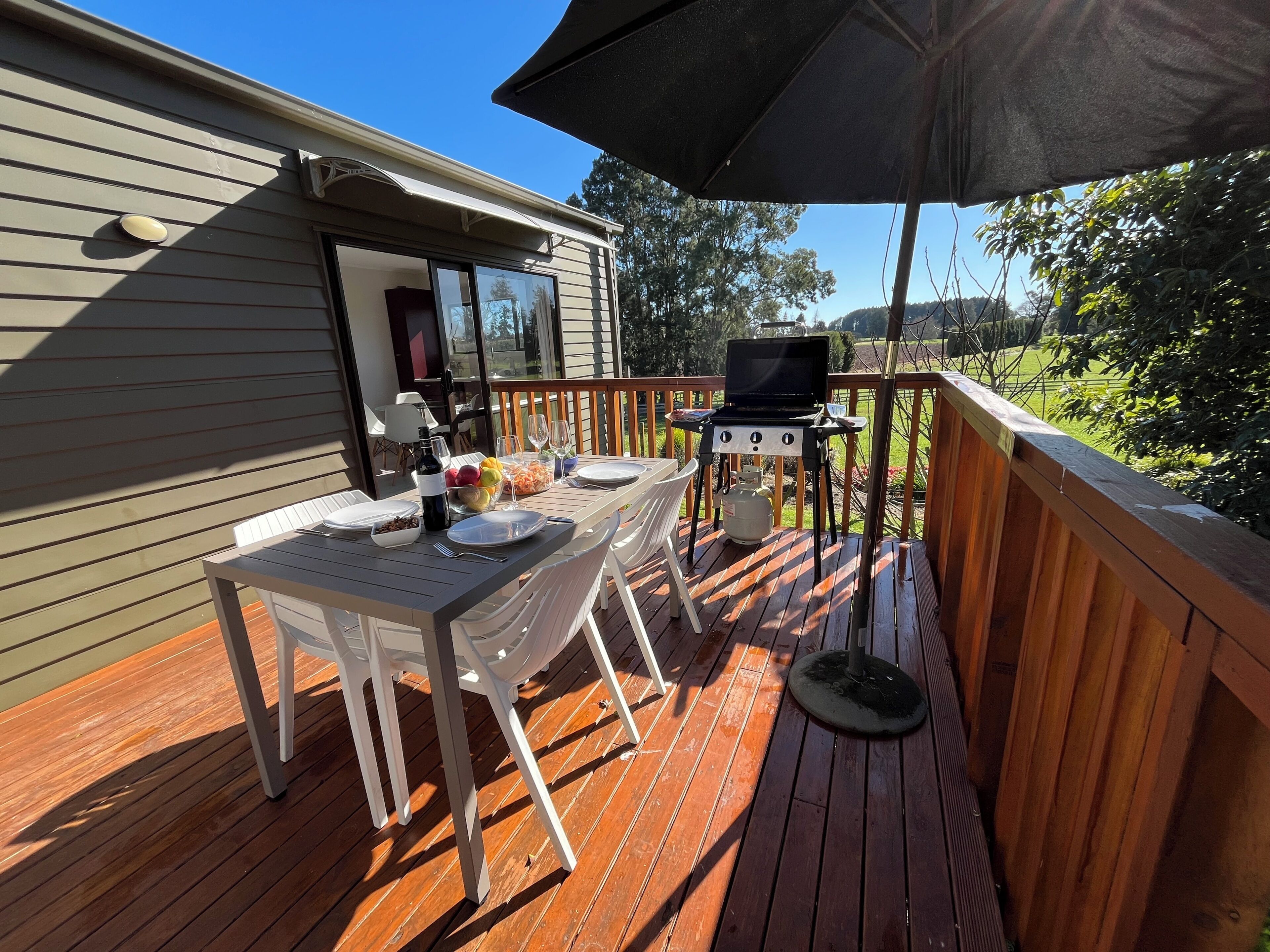 A wooden deck with a table set for dining, a grill, and an umbrella providing shade.