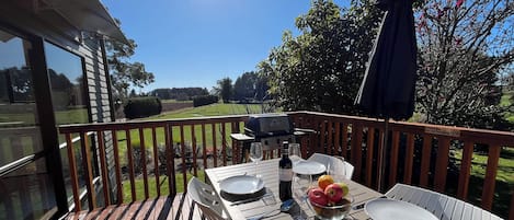 An outdoor dining area with a table set for two, a grill, and a view of the surrounding landscape.