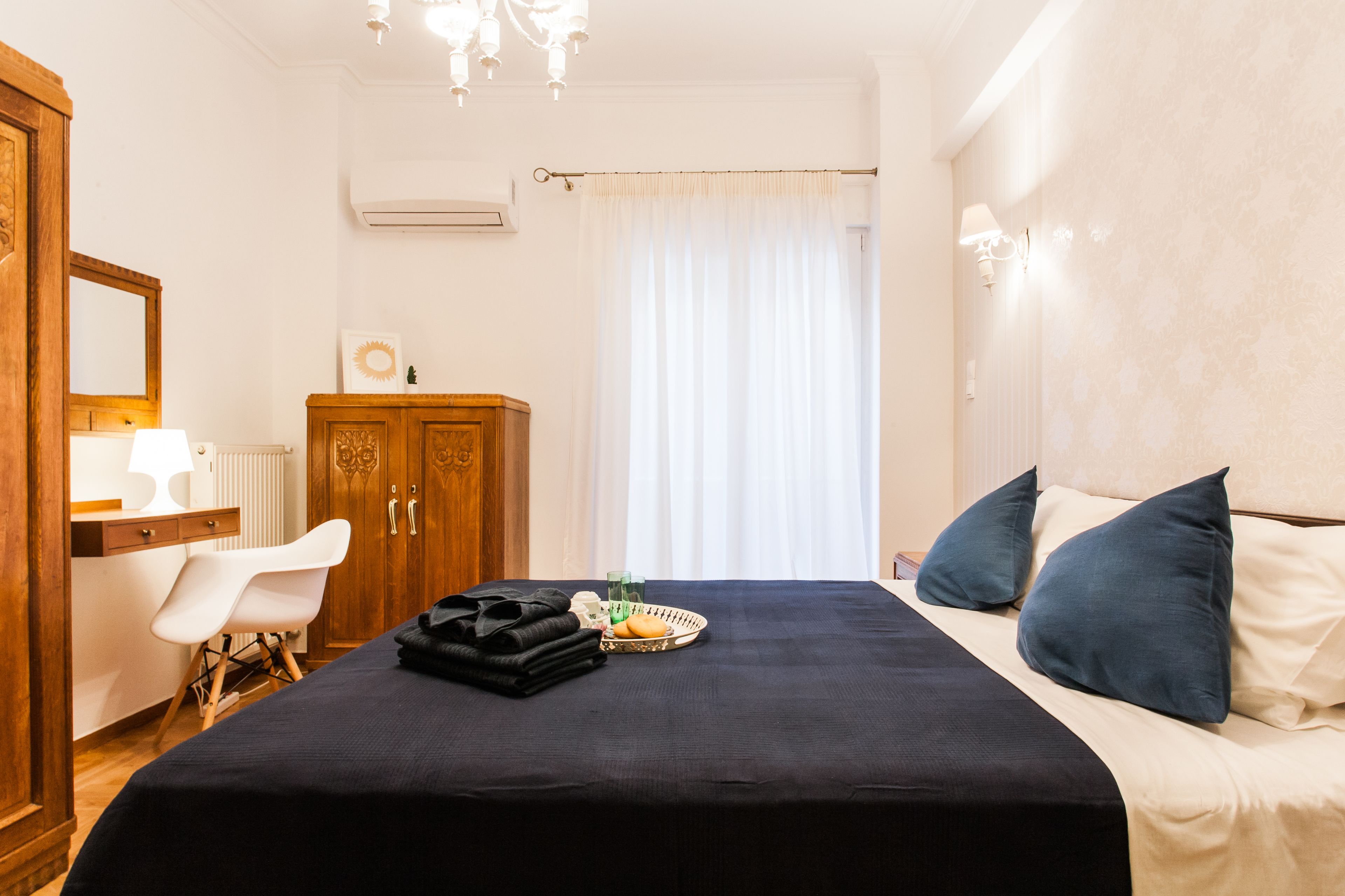 Une chambre d’hôtel avec un lit, une armoire en bois, un bureau avec une chaise et une fenêtre avec des rideaux.