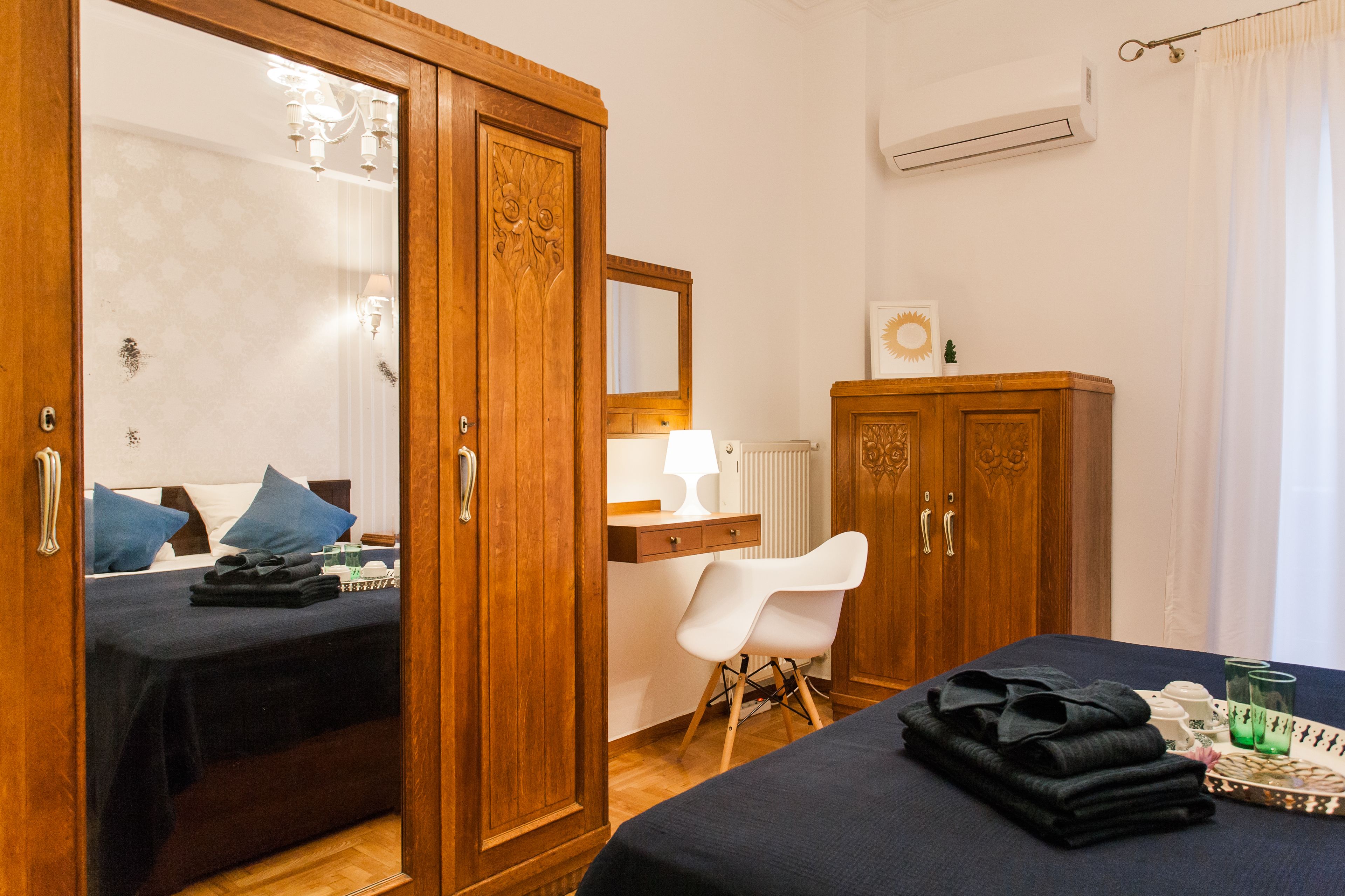 Une chambre d’hôtel comprenant un lit, une armoire en bois, un bureau avec une lampe, une chaise et une petite table avec des serviettes et des verres.