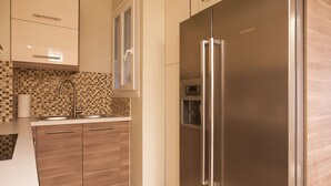 A modern kitchen with a stainless steel refrigerator, wooden cabinets, a tiled backsplash, and a window above the sink. - Gold and Blue Luxurious Apartment (Athens)