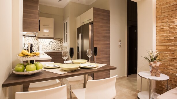 A modern kitchen with a dining area, featuring a wooden table set for four, white chairs, and a small round table with a decorative plant. - Gold and Blue Luxurious Apartment (Athens)