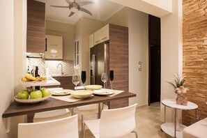 A modern kitchen with a dining area, featuring a wooden table set for four, white chairs, and a small round table with a decorative plant. - Gold and Blue Luxurious Apartment (Athens)