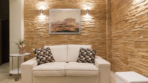 A beige sofa with checkered pillows, a small round table with a plant, and a framed picture of an ancient structure on a textured wall. - Gold and Blue Luxurious Apartment (Athens)